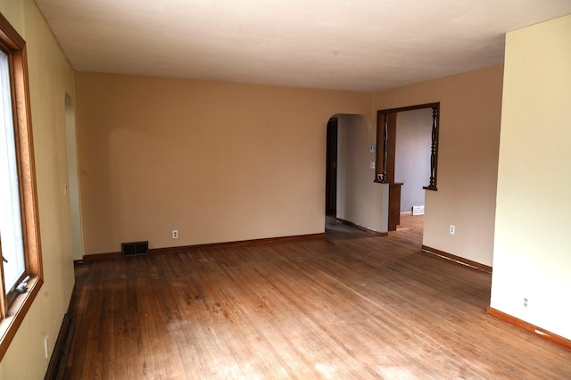 empty room with visible vents, baseboards, arched walkways, and wood finished floors