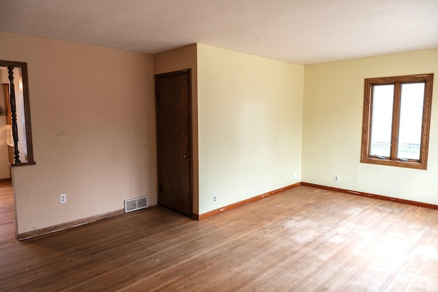 empty room with wood finished floors, baseboards, and visible vents