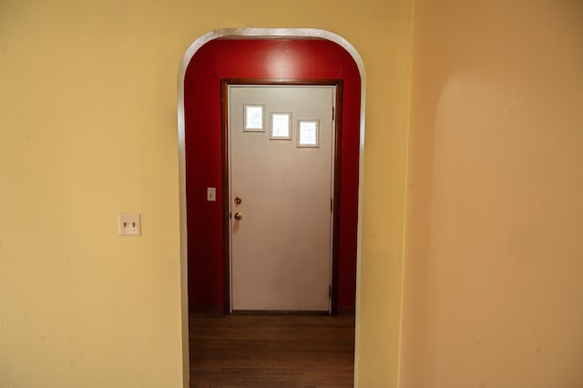 corridor with arched walkways, baseboards, and wood finished floors