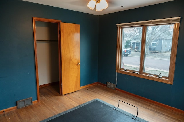 unfurnished bedroom featuring baseboards, wood finished floors, a closet, and visible vents