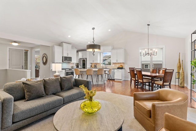 living area with light wood-style floors, an inviting chandelier, vaulted ceiling, and recessed lighting