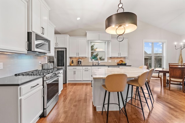 kitchen featuring appliances with stainless steel finishes, a center island, vaulted ceiling, and light wood finished floors