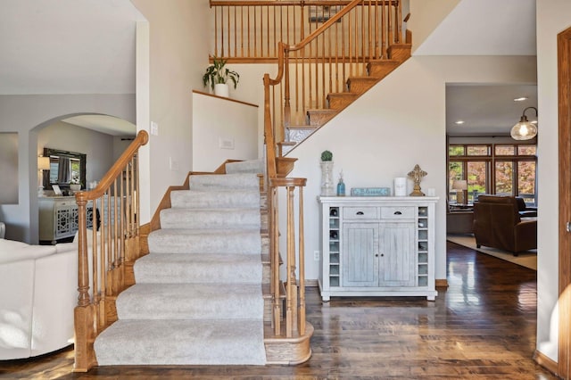 staircase featuring arched walkways and wood finished floors
