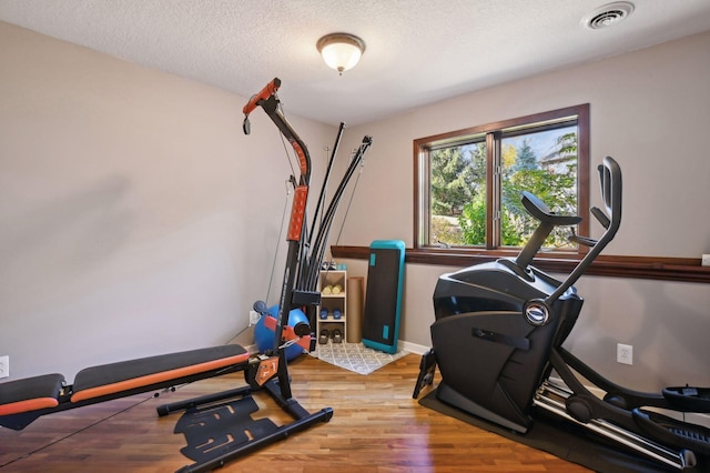 workout area with wood finished floors, visible vents, a textured ceiling, and baseboards