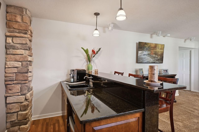 bar with dark wood finished floors, decorative light fixtures, a sink, baseboards, and a textured ceiling