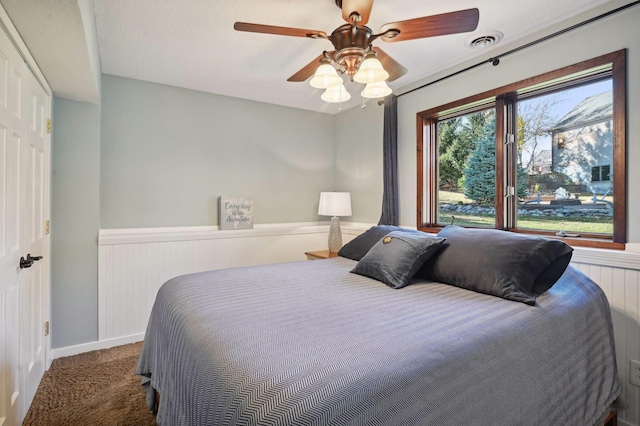 bedroom with ceiling fan, visible vents, wainscoting, and carpet floors