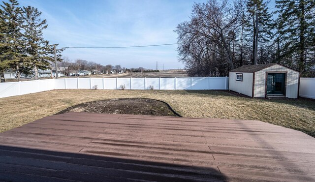 wooden deck featuring a lawn, a fenced backyard, a storage unit, and an outbuilding