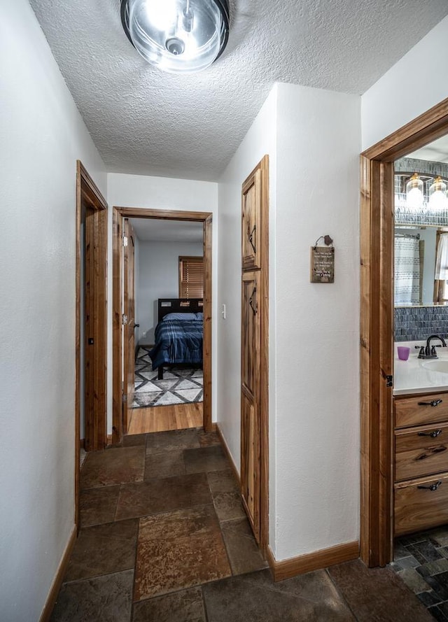 corridor with stone finish flooring, baseboards, a sink, and a textured ceiling