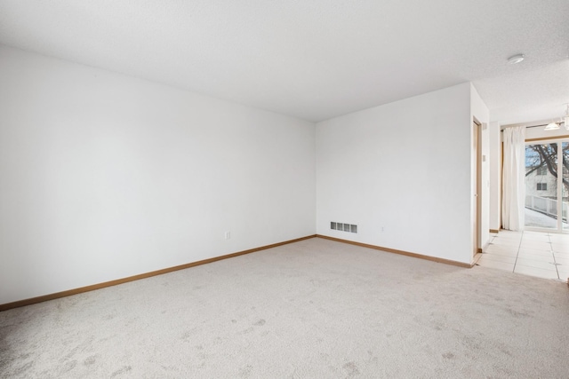 empty room featuring light colored carpet, visible vents, baseboards, and a textured ceiling