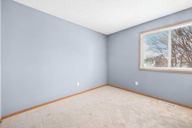 carpeted spare room with a textured ceiling, baseboards, and visible vents