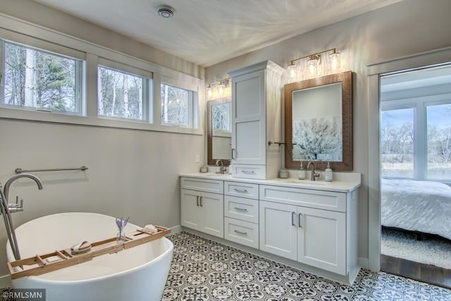 ensuite bathroom featuring a sink, baseboards, double vanity, and a soaking tub
