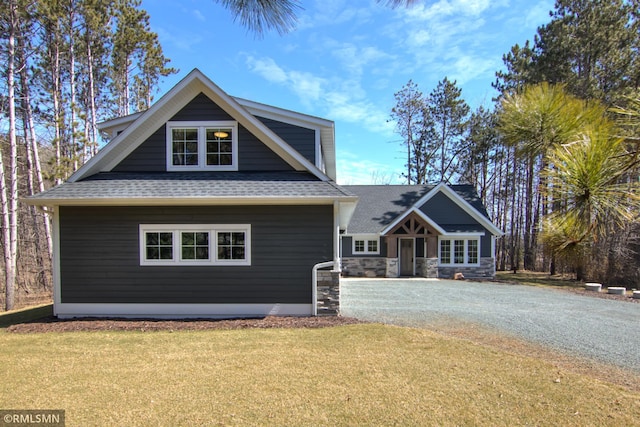 craftsman-style home featuring a shingled roof, a front yard, and driveway