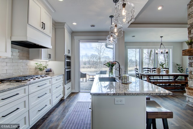 kitchen featuring a sink, appliances with stainless steel finishes, a chandelier, a breakfast bar area, and light stone counters