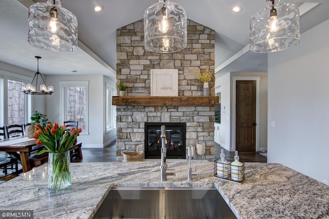 kitchen with a notable chandelier, a sink, wood finished floors, light stone countertops, and lofted ceiling