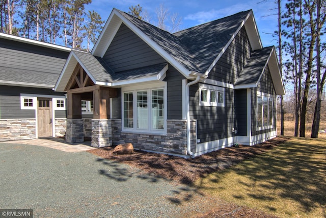 view of side of property featuring a yard, stone siding, and a shingled roof