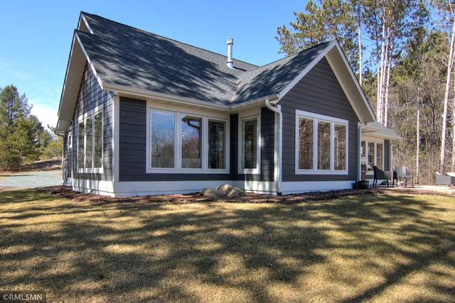 back of property with roof with shingles, a patio area, and a lawn