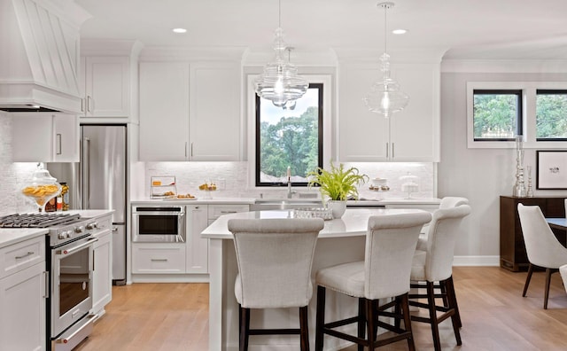 kitchen with light wood finished floors, white cabinets, appliances with stainless steel finishes, and premium range hood