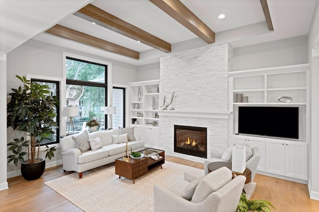 living area with light wood-type flooring, baseboards, built in shelves, beam ceiling, and a stone fireplace