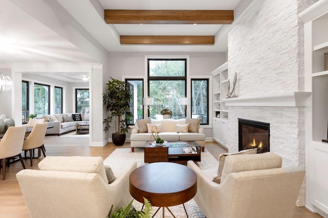 living area featuring a healthy amount of sunlight, a stone fireplace, light wood-style floors, and beamed ceiling