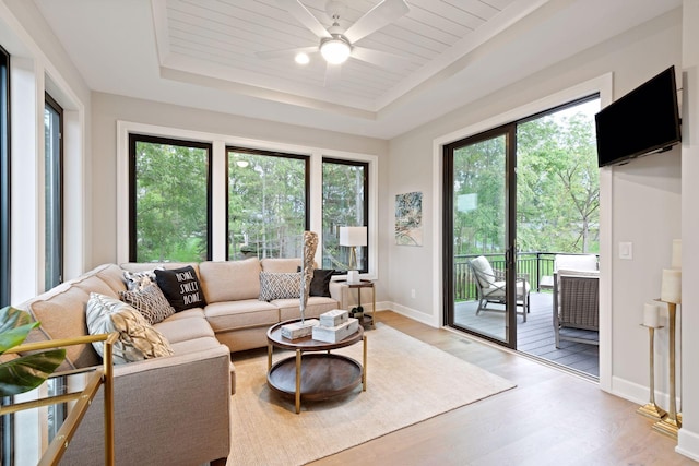 living area featuring a raised ceiling, plenty of natural light, light wood finished floors, and ceiling fan