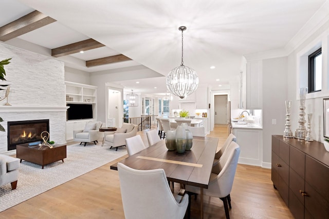 dining space with a stone fireplace, beam ceiling, an inviting chandelier, and light wood finished floors