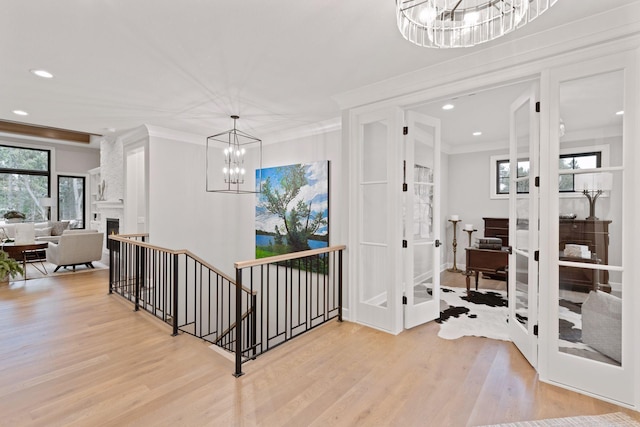 foyer featuring french doors, a fireplace, ornamental molding, light wood-style floors, and an inviting chandelier