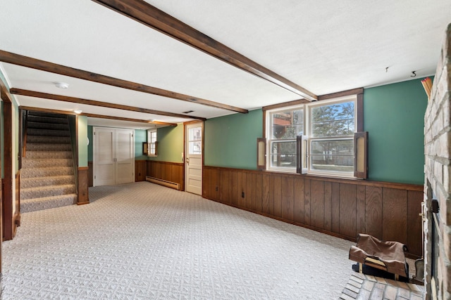 spare room featuring a large fireplace, a wainscoted wall, a baseboard heating unit, stairs, and beam ceiling