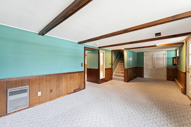 carpeted spare room with beamed ceiling, stairway, wainscoting, wooden walls, and heating unit