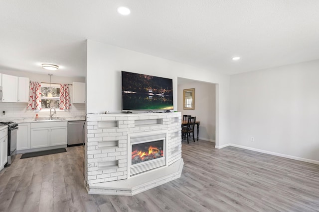 living area with a glass covered fireplace, recessed lighting, light wood-style flooring, and baseboards