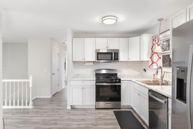 kitchen featuring stainless steel appliances, white cabinets, a sink, and backsplash
