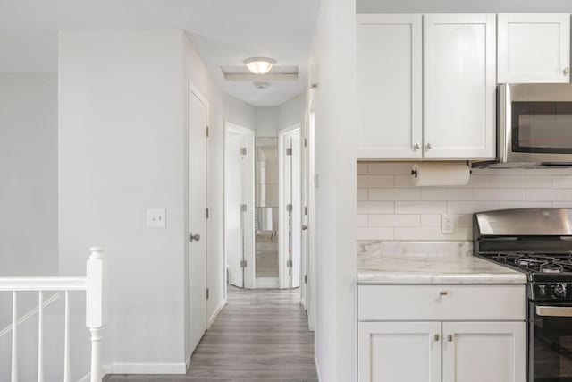 kitchen with stainless steel appliances, white cabinets, wood finished floors, and decorative backsplash