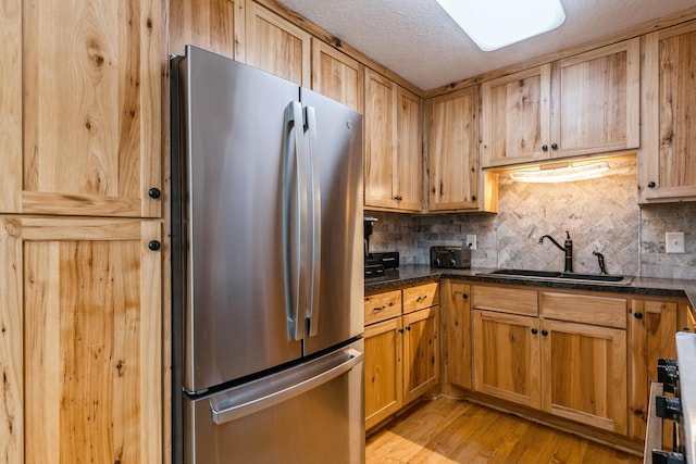 kitchen with tasteful backsplash, freestanding refrigerator, light wood-style floors, a sink, and a textured ceiling
