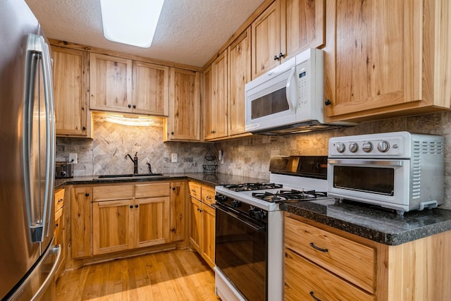 kitchen featuring range with gas stovetop, a sink, light wood-type flooring, white microwave, and freestanding refrigerator