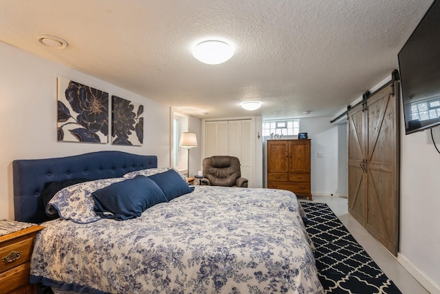 bedroom featuring a textured ceiling, a barn door, a closet, and baseboards