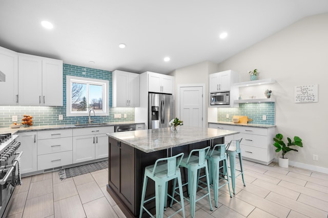 kitchen featuring open shelves, a sink, a breakfast bar area, backsplash, and appliances with stainless steel finishes