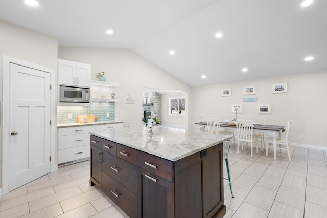 kitchen with vaulted ceiling, tasteful backsplash, stainless steel microwave, white cabinetry, and a kitchen island