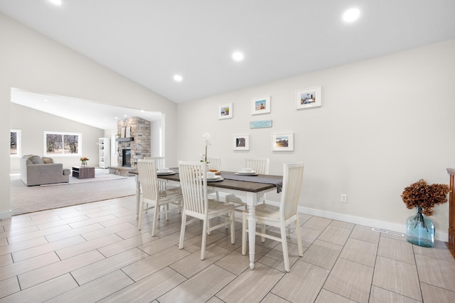 dining space featuring recessed lighting, wood tiled floor, vaulted ceiling, a stone fireplace, and baseboards