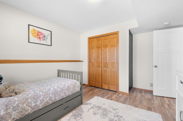 bedroom featuring baseboards, wood finished floors, visible vents, and a closet
