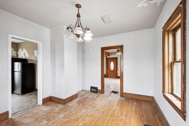 spare room featuring light wood-style flooring, plenty of natural light, a chandelier, and baseboards