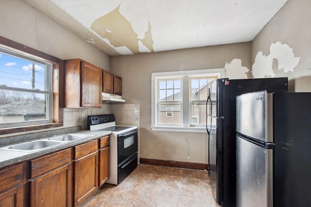 kitchen with range with electric stovetop, freestanding refrigerator, brown cabinetry, under cabinet range hood, and healthy amount of natural light