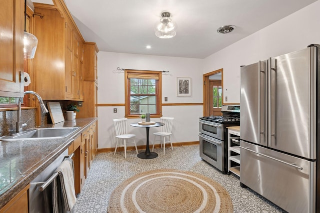 kitchen with stainless steel appliances, a sink, brown cabinets, and baseboards