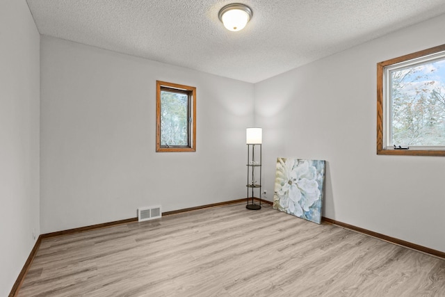 spare room with baseboards, a textured ceiling, visible vents, and light wood finished floors