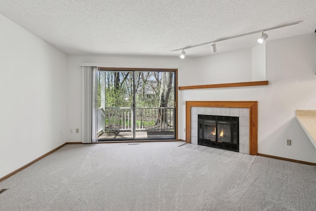 unfurnished living room featuring a tiled fireplace, track lighting, carpet flooring, and a textured ceiling