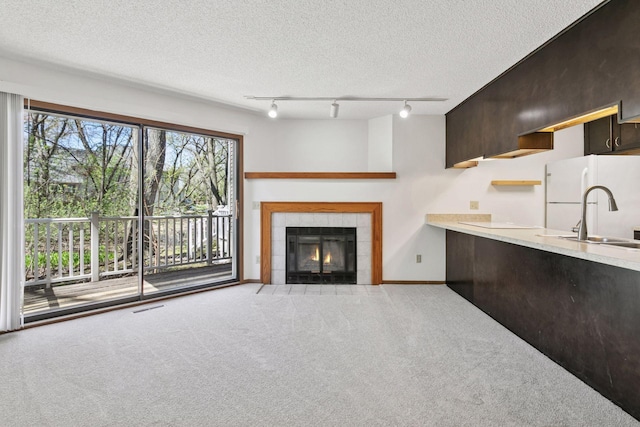 unfurnished living room with a sink, carpet floors, a tiled fireplace, baseboards, and visible vents