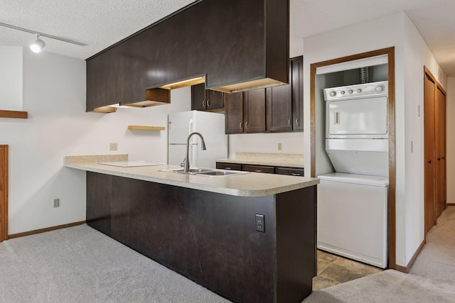 kitchen featuring stacked washer and clothes dryer, a peninsula, dark brown cabinetry, light colored carpet, and a sink