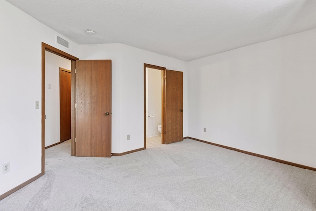 unfurnished bedroom with light colored carpet, baseboards, visible vents, and ensuite bath