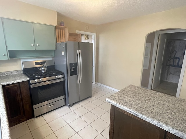 kitchen with light tile patterned flooring, appliances with stainless steel finishes, light countertops, arched walkways, and a textured ceiling