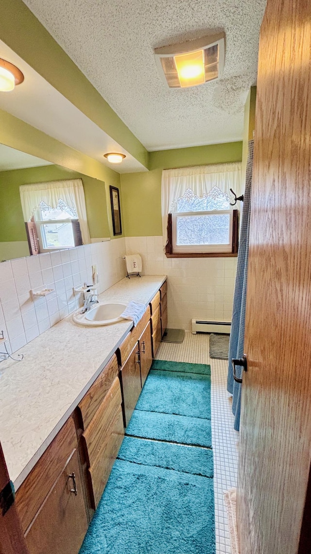 bathroom with visible vents, tile walls, a textured ceiling, vanity, and a baseboard heating unit