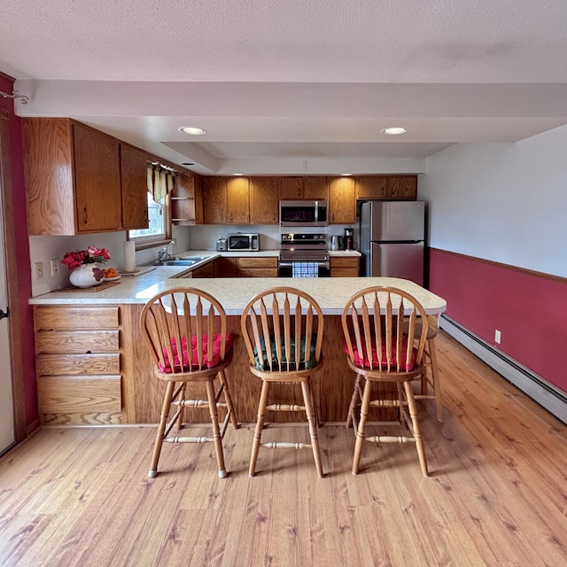 kitchen featuring a peninsula, light wood-style flooring, light countertops, brown cabinetry, and stainless steel appliances