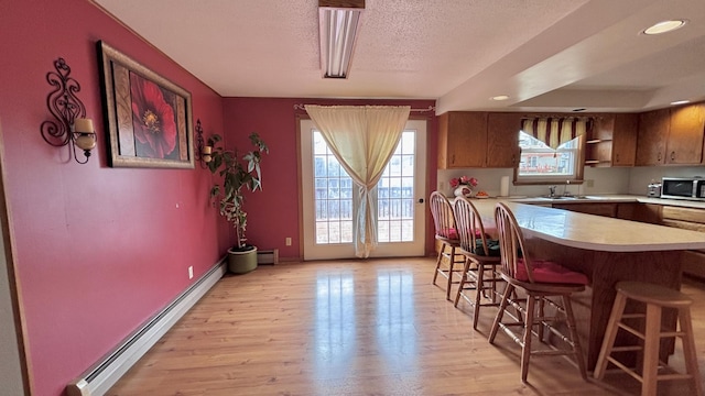 dining room featuring a baseboard heating unit, baseboards, light wood-type flooring, a textured ceiling, and a baseboard radiator